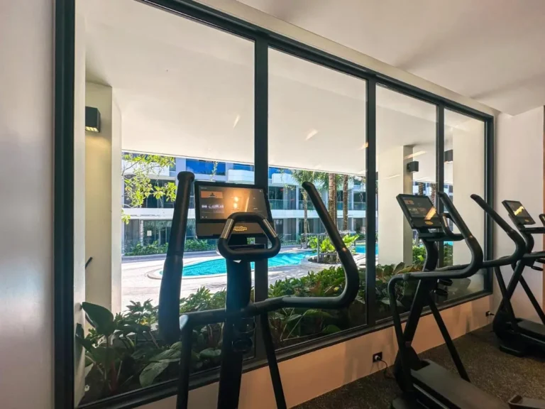 Indoor Gym with Elliptical Machines Overlooking Curved Swimming Pool and Tropical Landscape