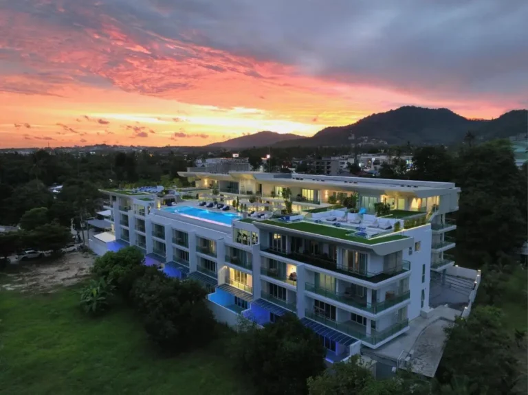 Modern Multi-Story Building with Illuminated Rooftop Pool and Scenic Sunset Views at Rawai Beach