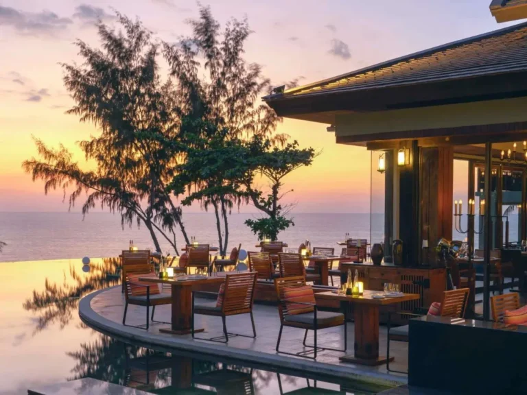 Outdoor Dining Area with Curved Infinity Pool Overlooking Ocean at Sunset