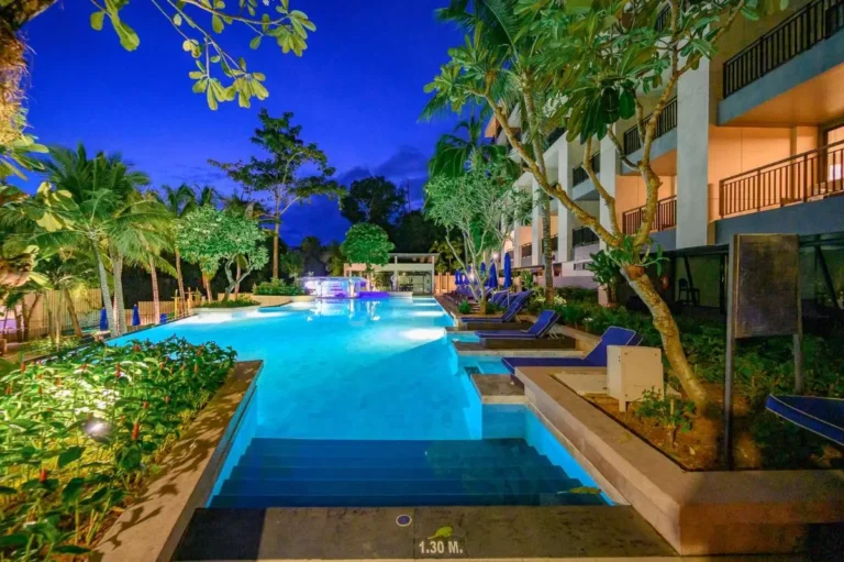 Outdoor Rectangular Swimming Pool with Lounge Chairs and Tropical Landscaping at Night in Kata Beach
