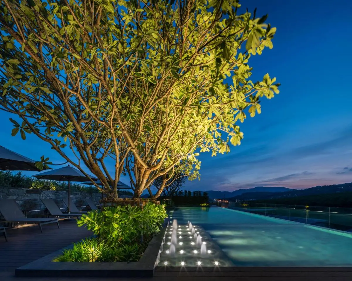 Tranquil Outdoor Infinity Pool with Illuminated Water Jets and Wooden Deck in Phuket Town